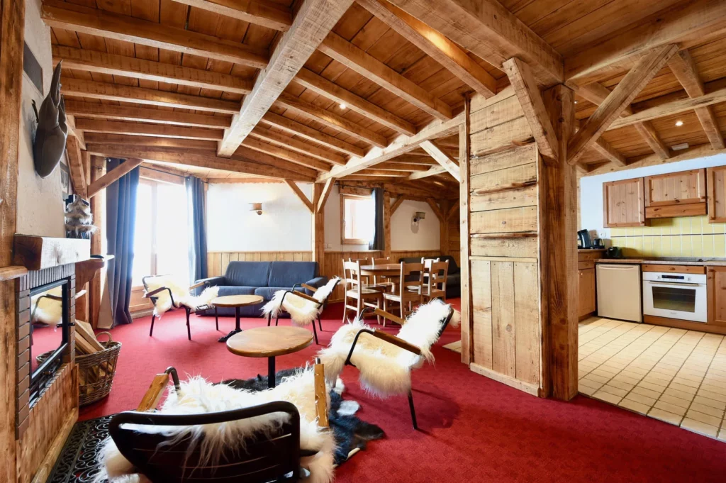 Salon avec cheminée, fauteuils en peau de mouton et cuisine en arrière-plan dans l'appartement standard plain-pied 6 personnes des Ancolies