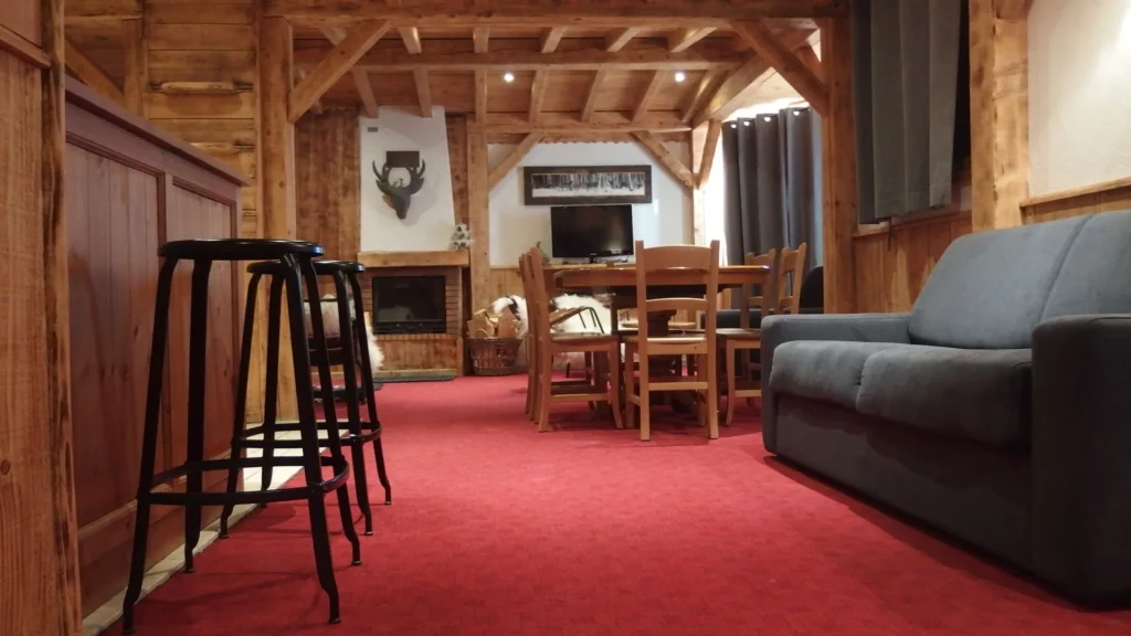 Salon avec tabourets de bar, tapis rouge et télévision dans l'appartement standard plain-pied 6 personnes des Ancolies
